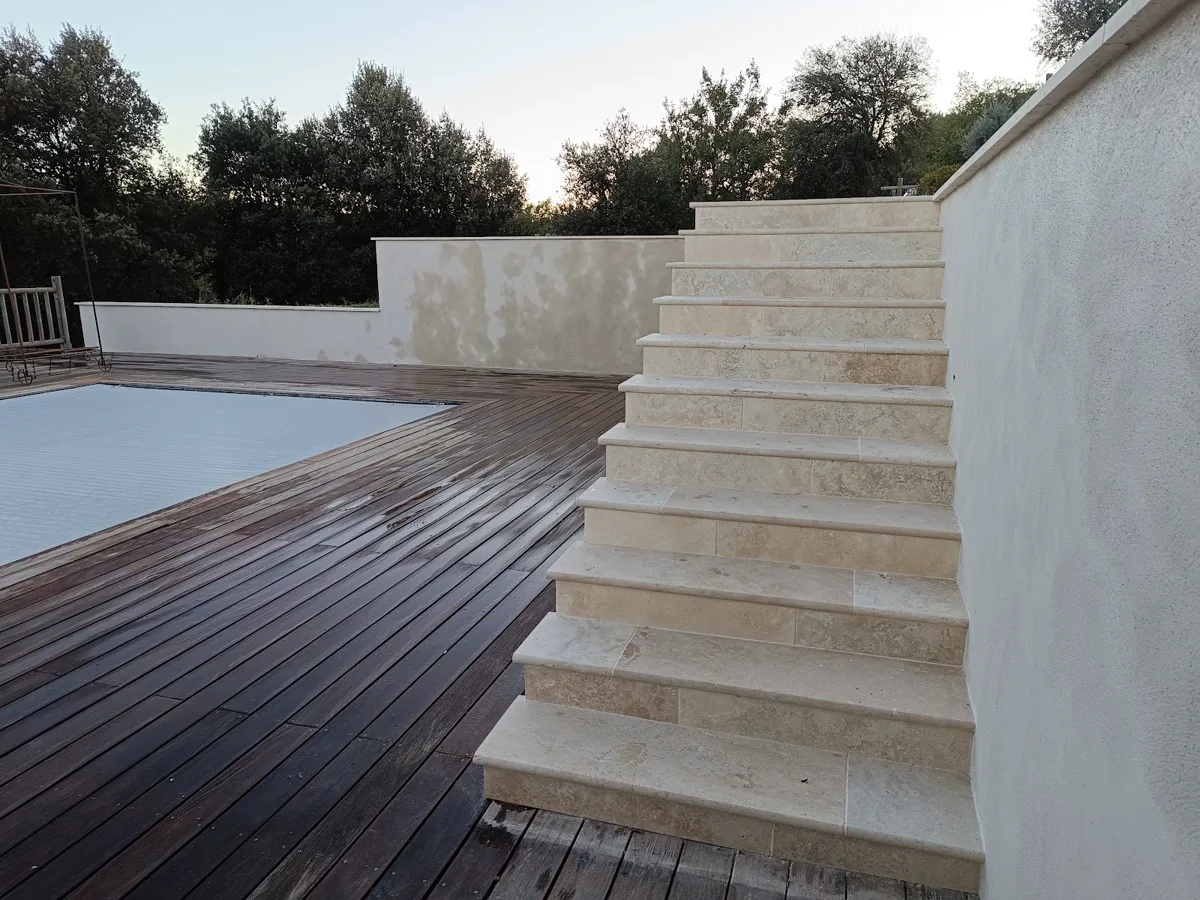 Escalier en pierre descendant vers une plage de piscine et une terrasse en bois