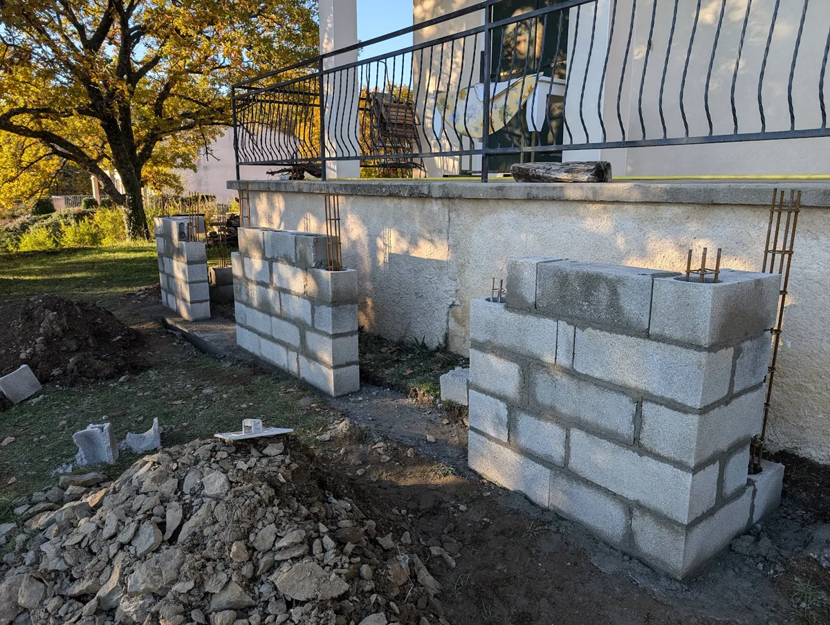 Piliers en parpaing ferraillés en cours de montage le long d'un mur